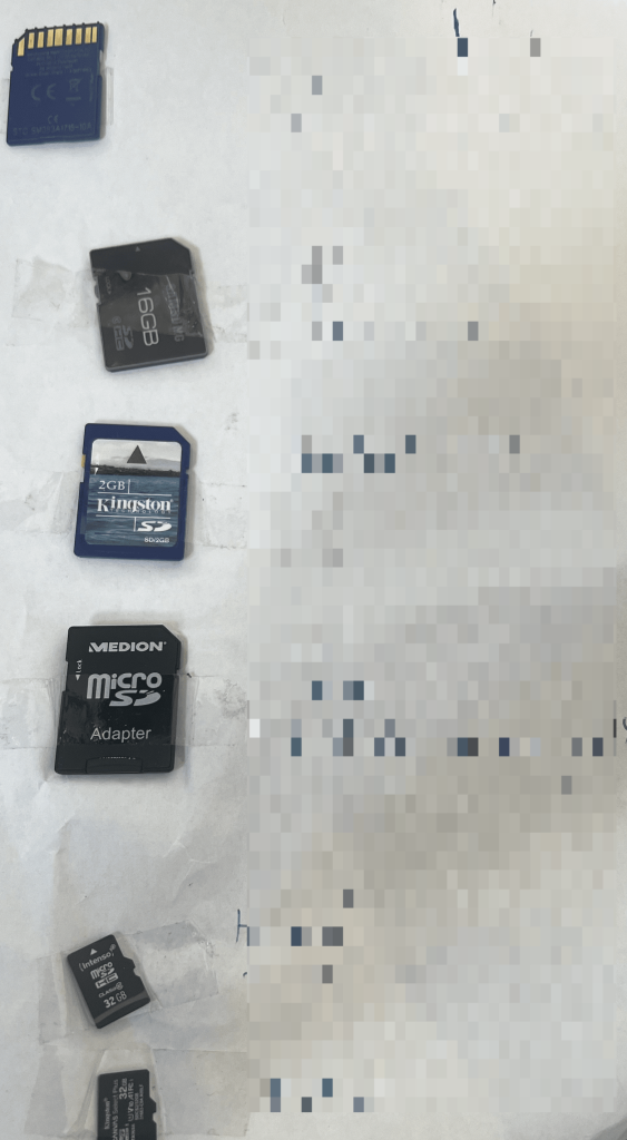 A picture of multiple SD cards being taped on white paper. The description next to it was blurred. 